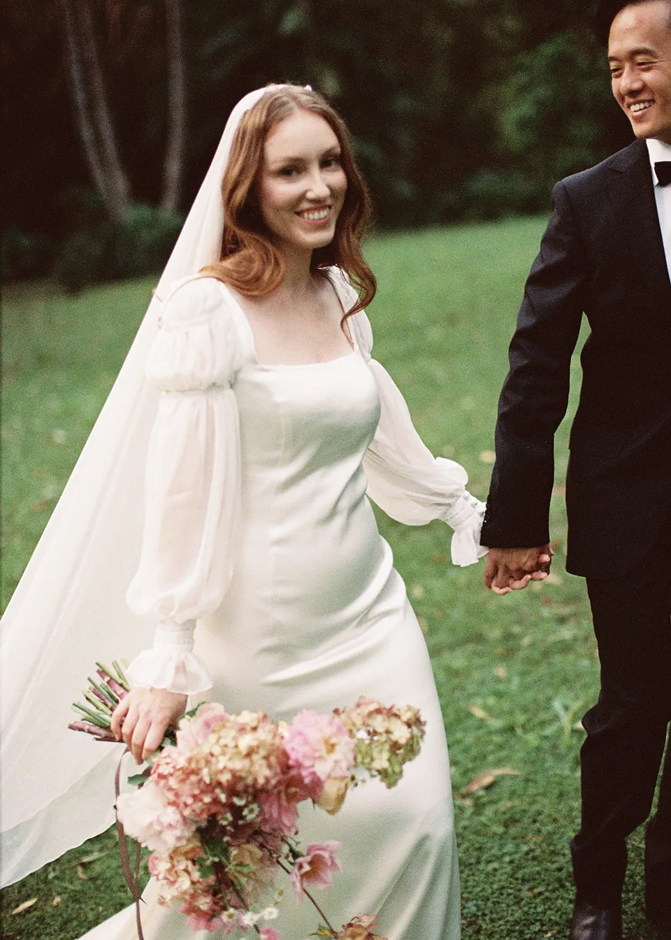 On 35mm film: Elyse smiling as Jonathan holds her hand in the garden. At Fig Tree Villa in Ewingsdale, Byron Bay, for an Elopement Collective elopement. Photograph by Bulb Creative.