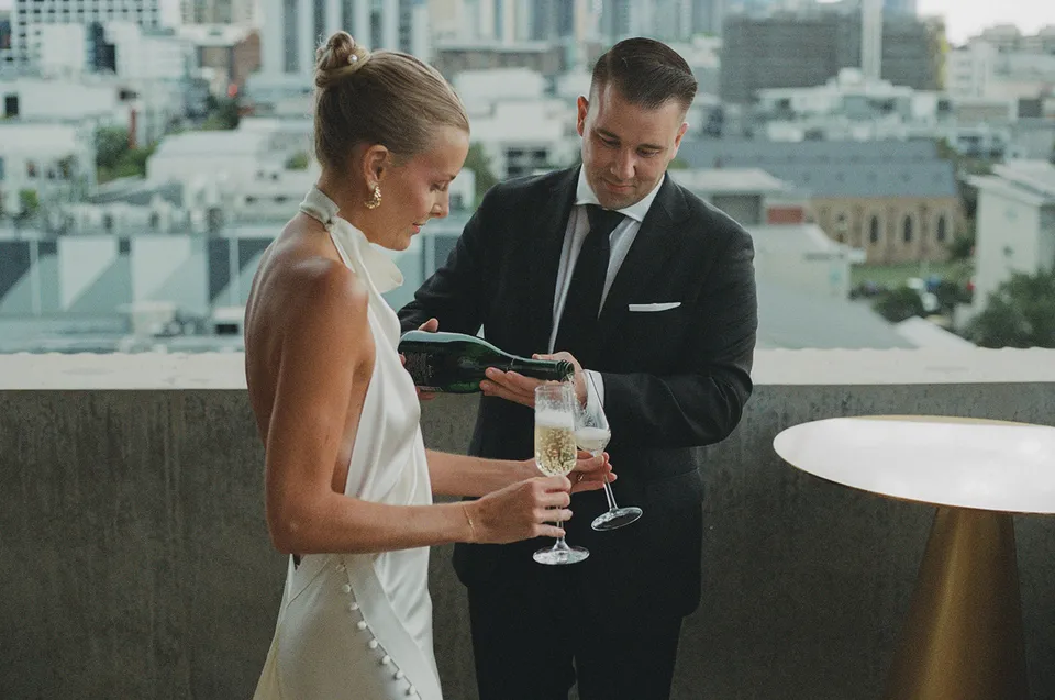 Matt reading from a green vow booklet beside Clare on The Calile Hotel terrace in Fortitude Valley during their Elopement Collective elopement in Brisbane.