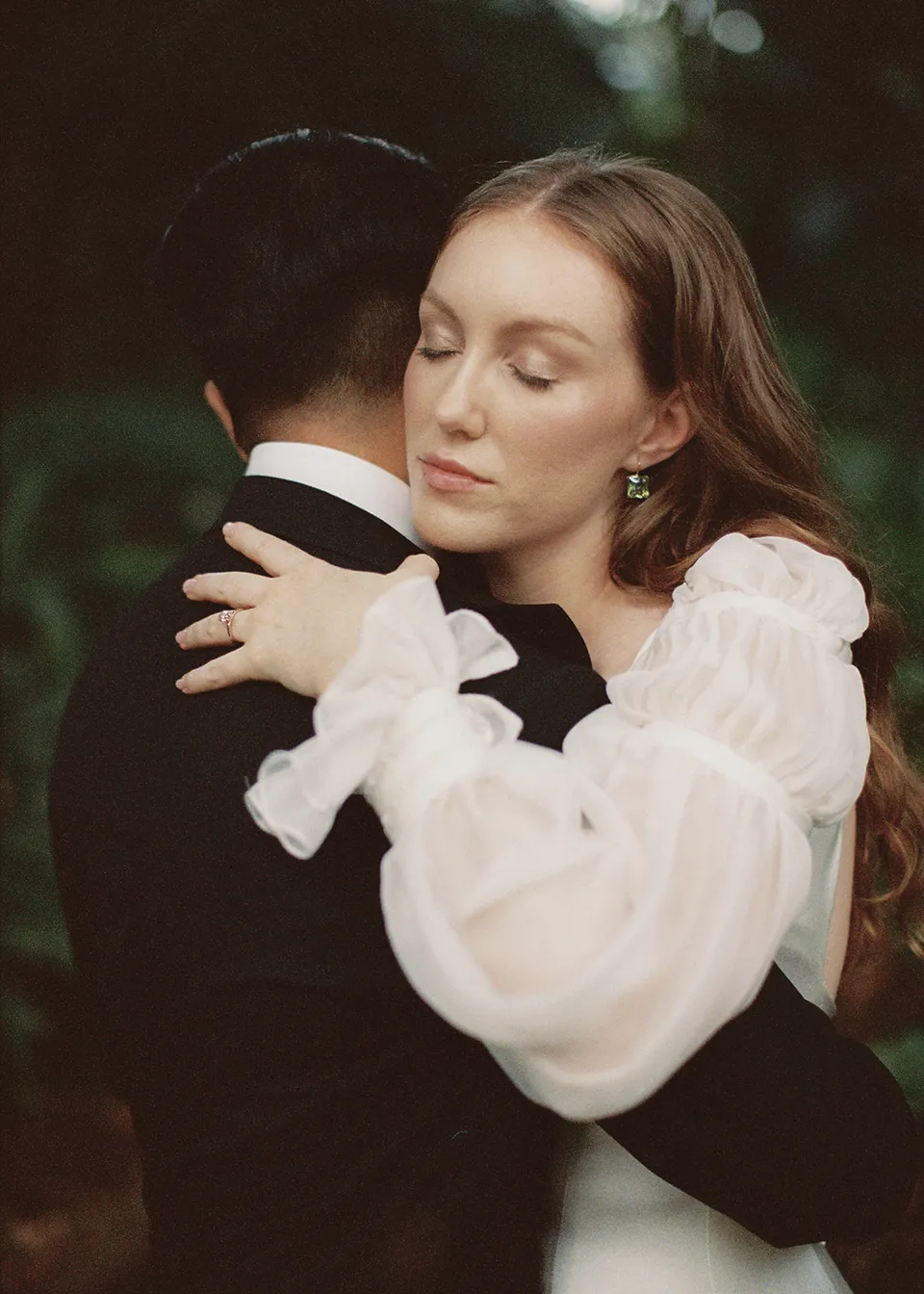 On 35mm film: Elyse resting her head on Jonathan's shoulder as they embrace. At Fig Tree Villa in Ewingsdale, Byron Bay, for an Elopement Collective elopement. Photograph by Bulb Creative.