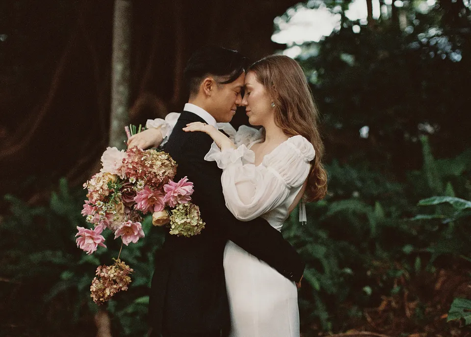 On 35mm film: The couple leaning their foreheads together with the pink bouquet over Jonathan's shoulder, with flowers by The Perfect Party Co. At Fig Tree Villa in Ewingsdale, Byron Bay, for an Elopement Collective elopement. Photograph by Bulb Creative.