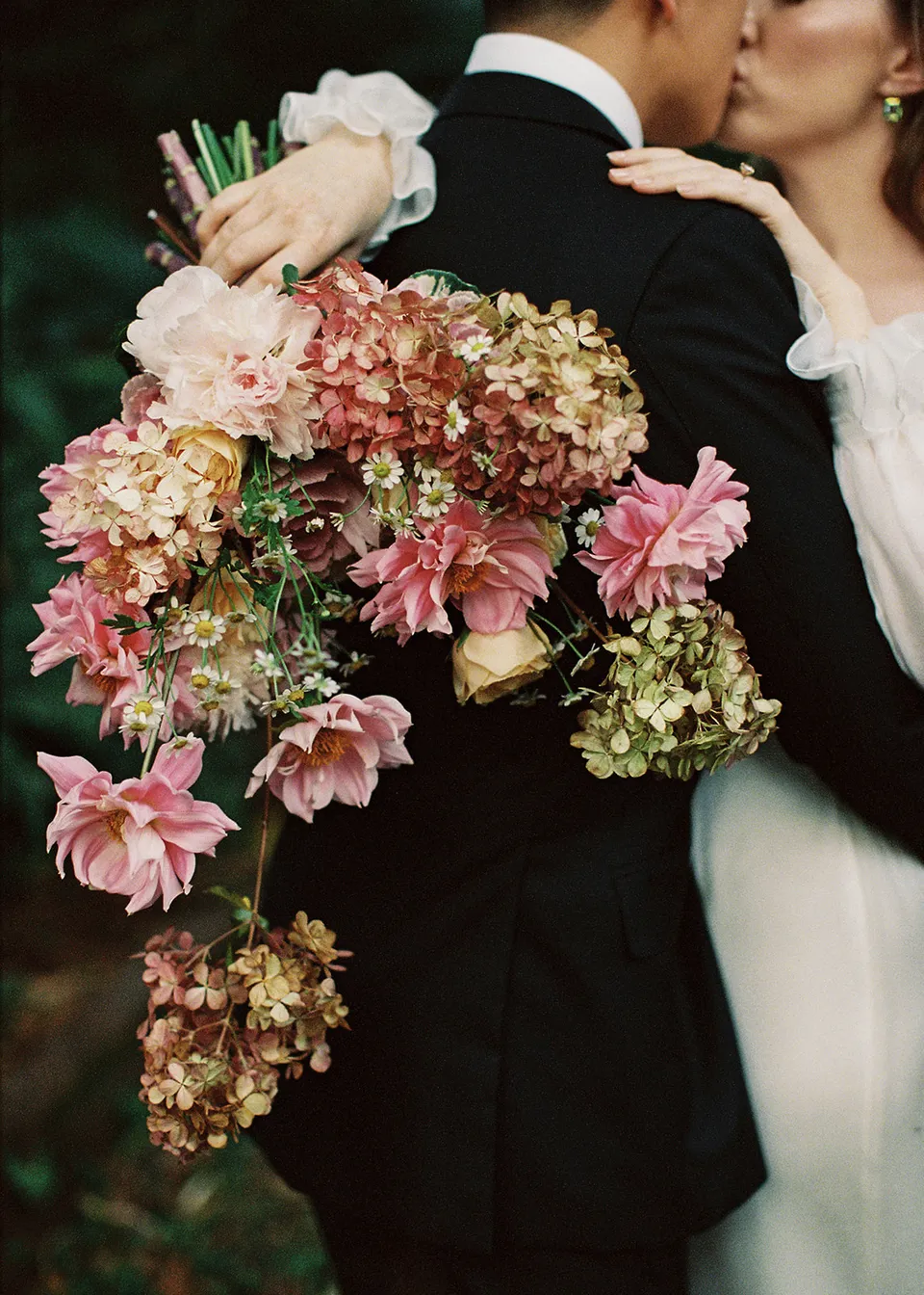 On 35mm film: Close-up of the pink bouquet and Elyse's hands around Jonathan's shoulders, with flowers by The Perfect Party Co. At Fig Tree Villa in Ewingsdale, Byron Bay, for an Elopement Collective elopement. Photograph by Bulb Creative.