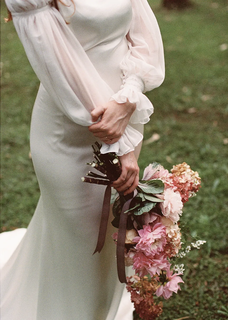 On 35mm film: Detail of Elyse's hands, dress cuffs and bouquet stems, with flowers by The Perfect Party Co. At Fig Tree Villa in Ewingsdale, Byron Bay, for an Elopement Collective elopement. Photograph by Bulb Creative.