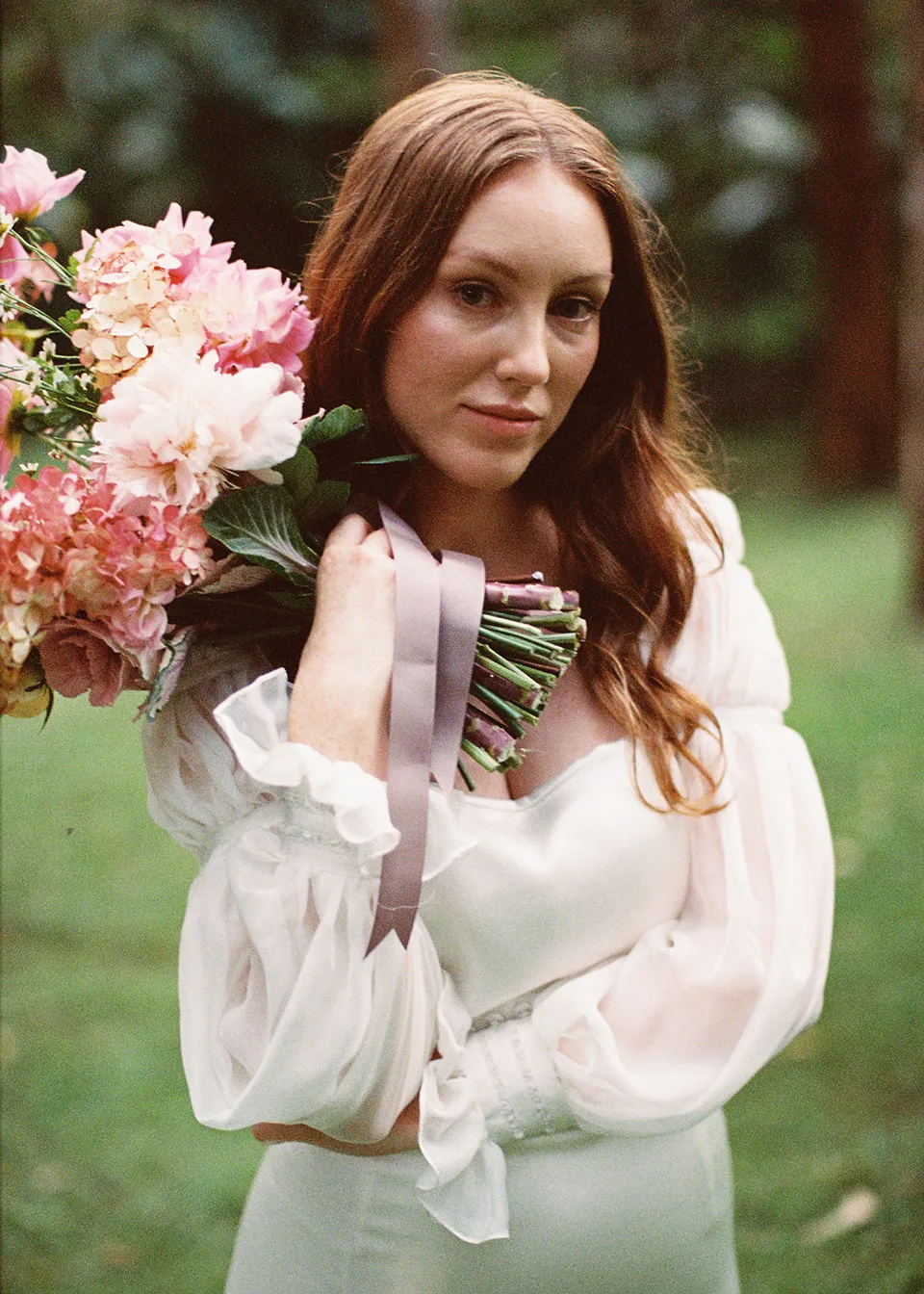 On 35mm film: Close portrait of Elyse with her bouquet resting beside her face, with flowers by The Perfect Party Co. At Fig Tree Villa in Ewingsdale, Byron Bay, for an Elopement Collective elopement. Photograph by Bulb Creative.