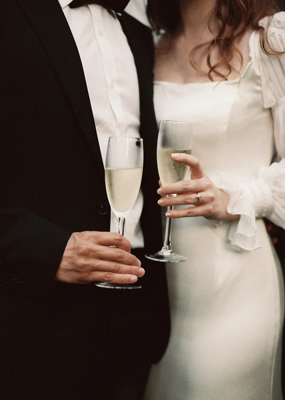 On 35mm film: Close-up of Elyse and Jonathan holding sparkling-wine glasses. At Fig Tree Villa in Ewingsdale, Byron Bay, for an Elopement Collective elopement. Photograph by Bulb Creative.