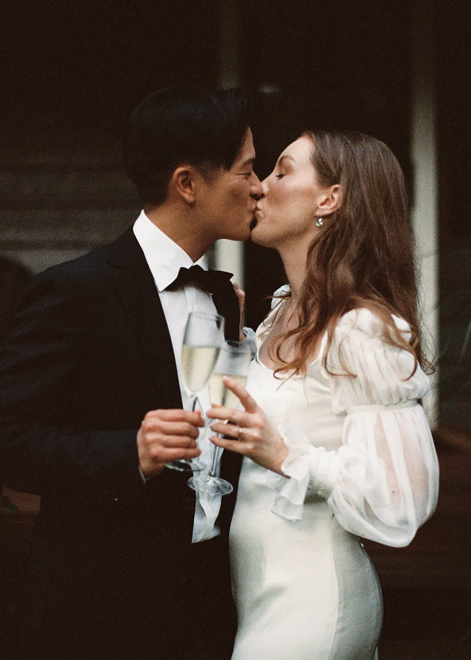 On 35mm film: a close portrait of the couple sharing a celebratory kiss outside the cottage. At Fig Tree Villa in Ewingsdale, Byron Bay, for an Elopement Collective elopement. Photograph by Bulb Creative.