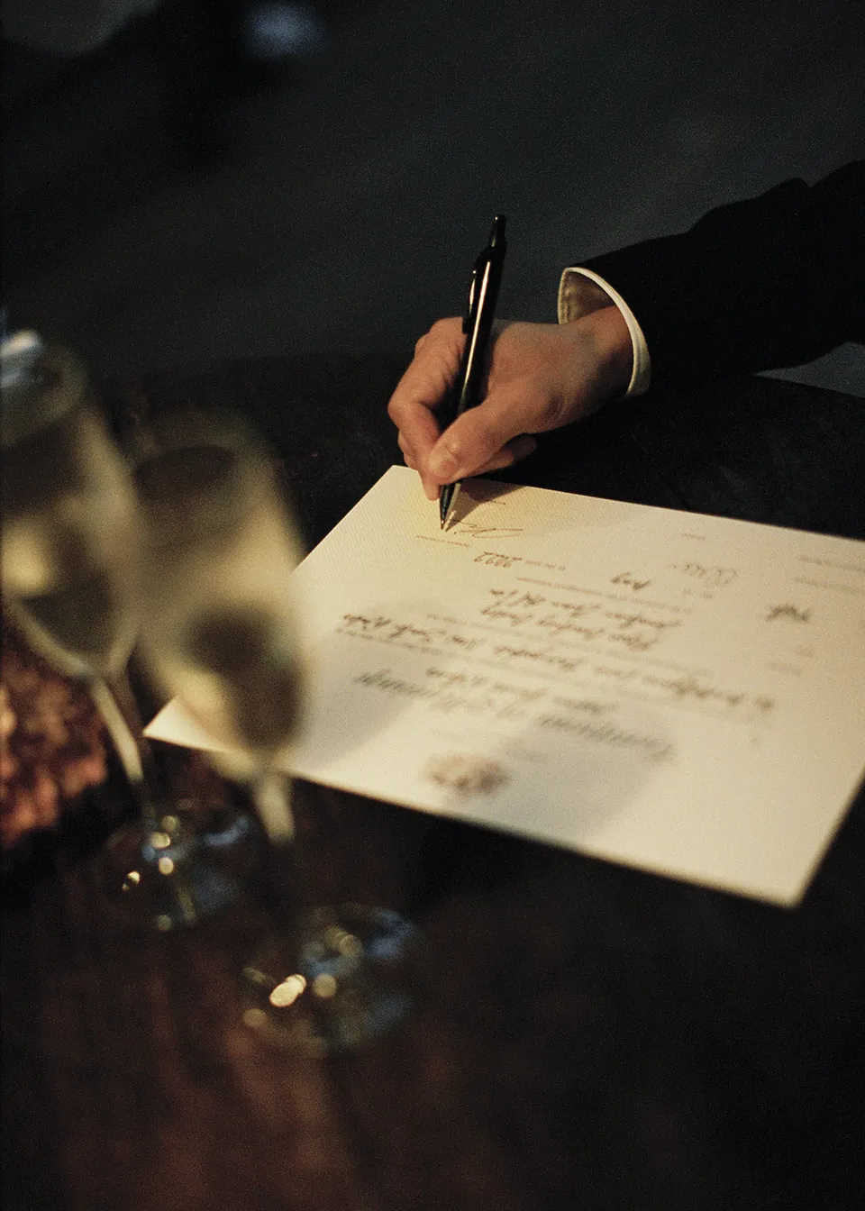 On 35mm film: Close-up of a hand signing the couple's ceremony paperwork. At Fig Tree Villa in Ewingsdale, Byron Bay, for an Elopement Collective elopement. Photograph by Bulb Creative.