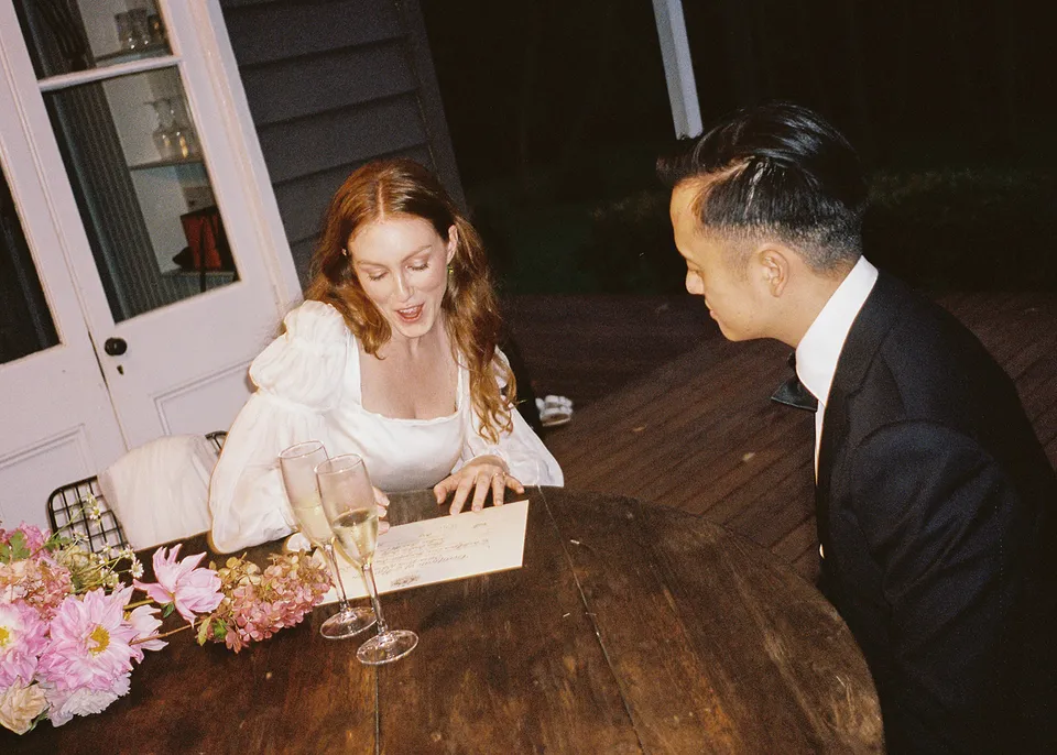 On 35mm film: Elyse smiling while signing paperwork at the outdoor timber table. At Fig Tree Villa in Ewingsdale, Byron Bay, for an Elopement Collective elopement. Photograph by Bulb Creative.