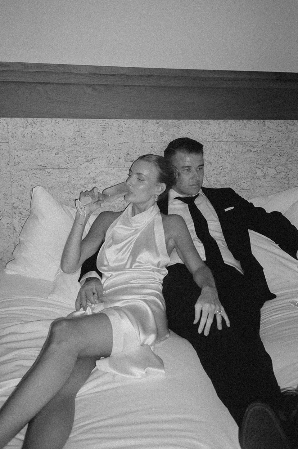 Black and white film photograph of Clare sipping champagne beside Matt on a sofa at The Calile Hotel, Fortitude Valley, during their Elopement Collective Brisbane elopement.