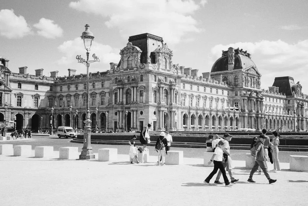 Black and white photo of the Louvre Museum in Paris, with people walking in the foreground.