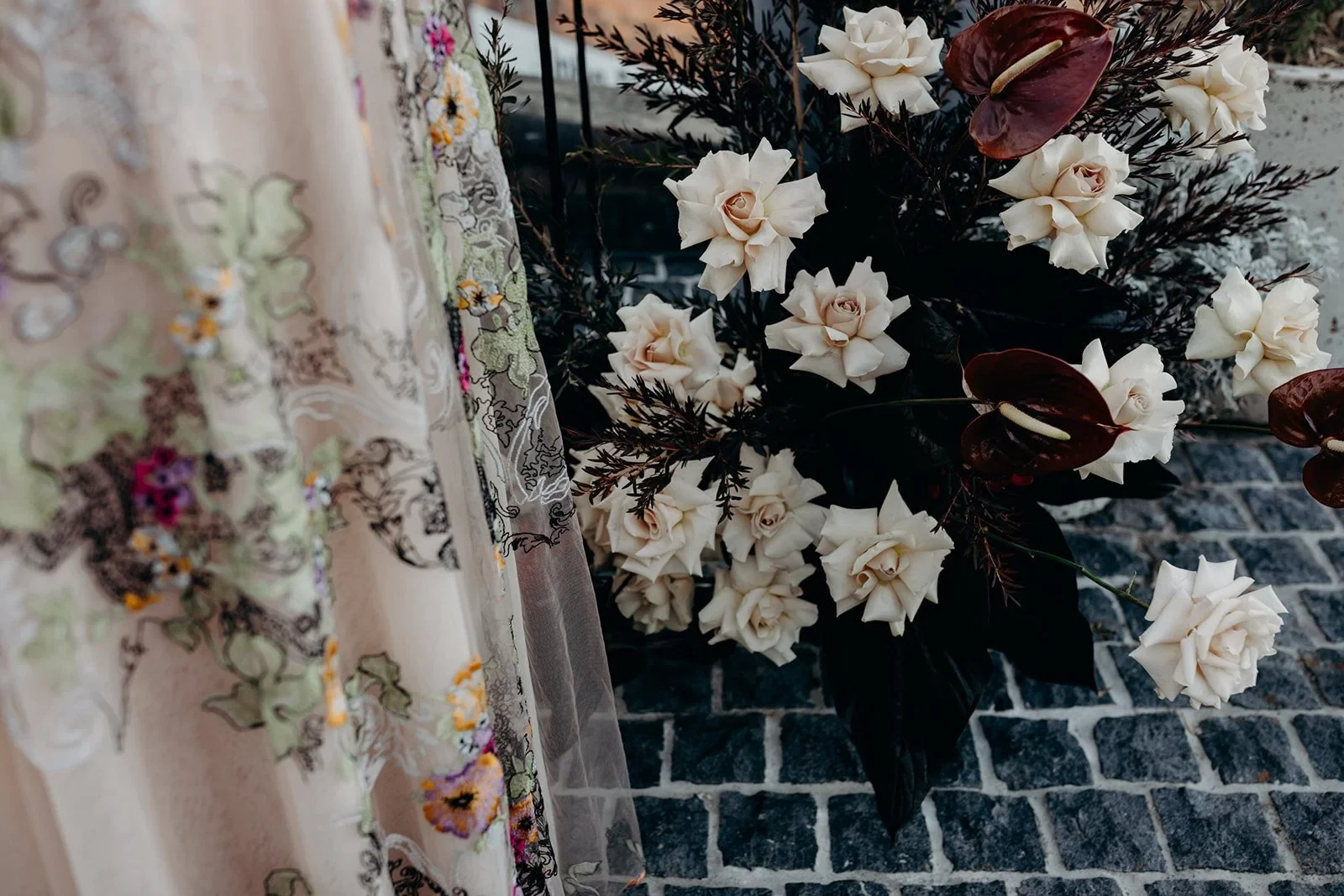 Detail of Victoria’s floral dress beside white blooms and burgundy flowers arranged by Mrs Gibbons Flowers, at Agnes Restaurant in Fortitude Valley, Brisbane, for an Elopement Collective elopement. Photo by Tessa Shannon.