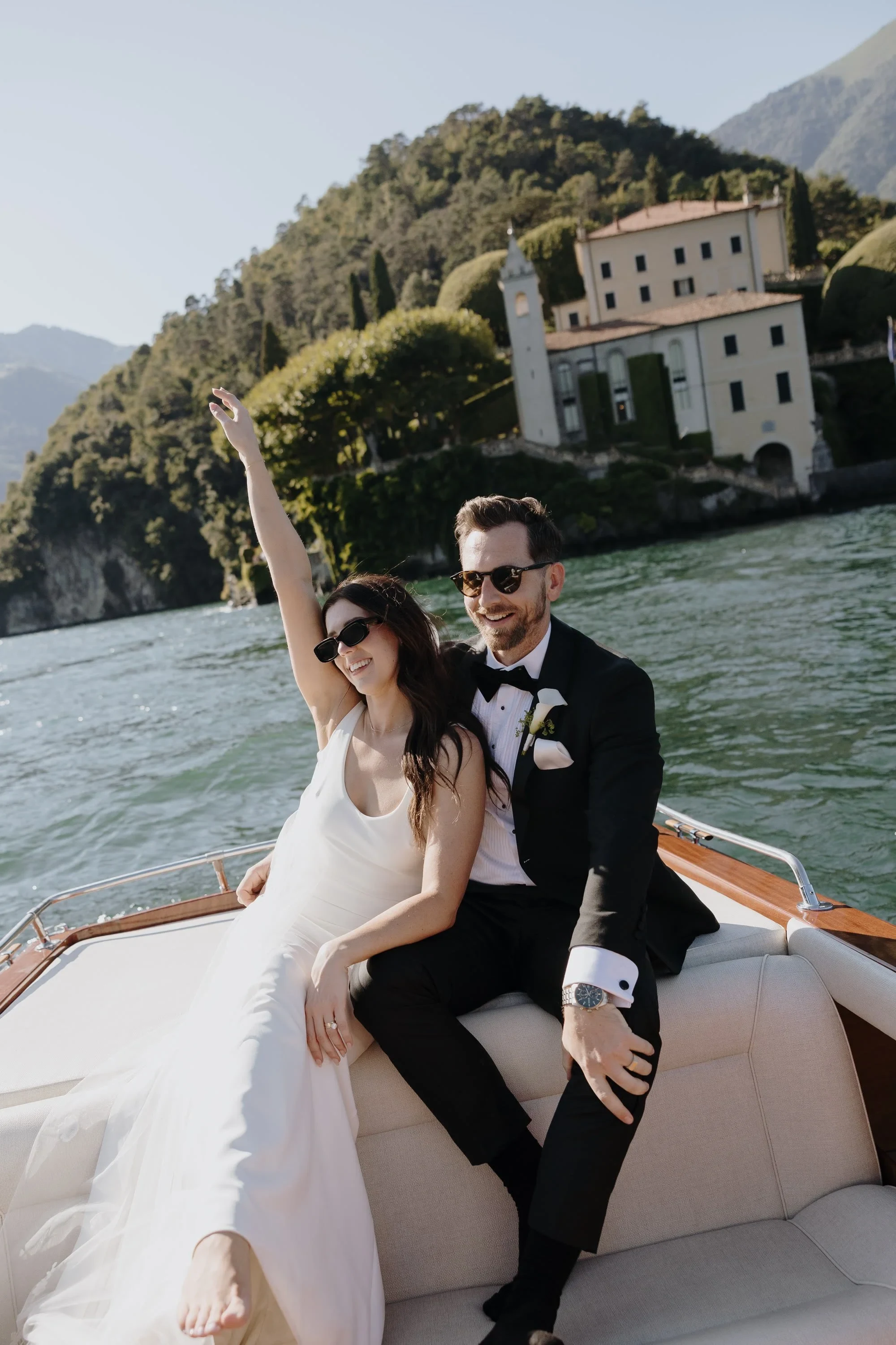 Couple in wedding attire seated in a wooden boat on a mountain lake