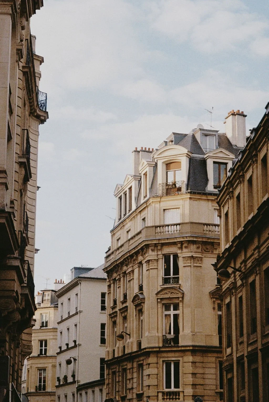 Classic Parisian architecture with ornate facade and mansard roof, viewed from a narrow street against a blue sky.