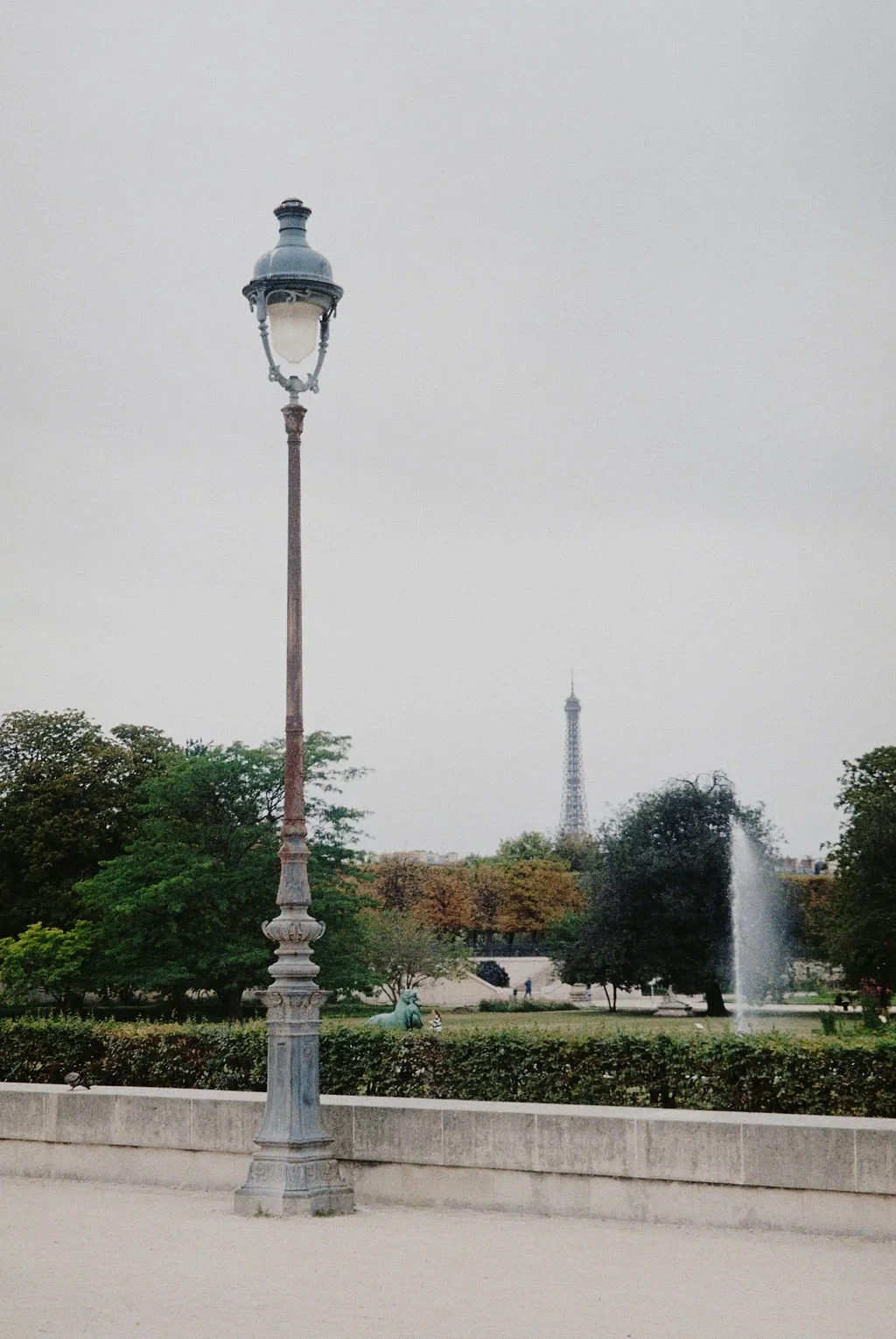 Vintage street lamp with Eiffel Tower in background, Paris park, cloudy sky.