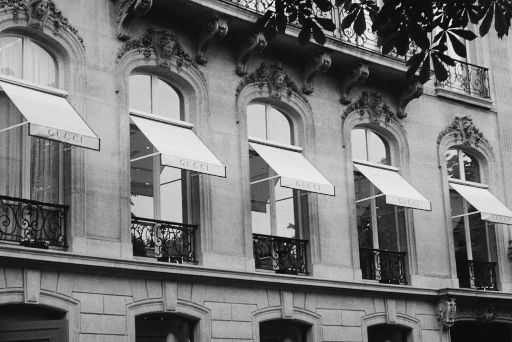 Facade of a Gucci store with ornate windows and white awnings.