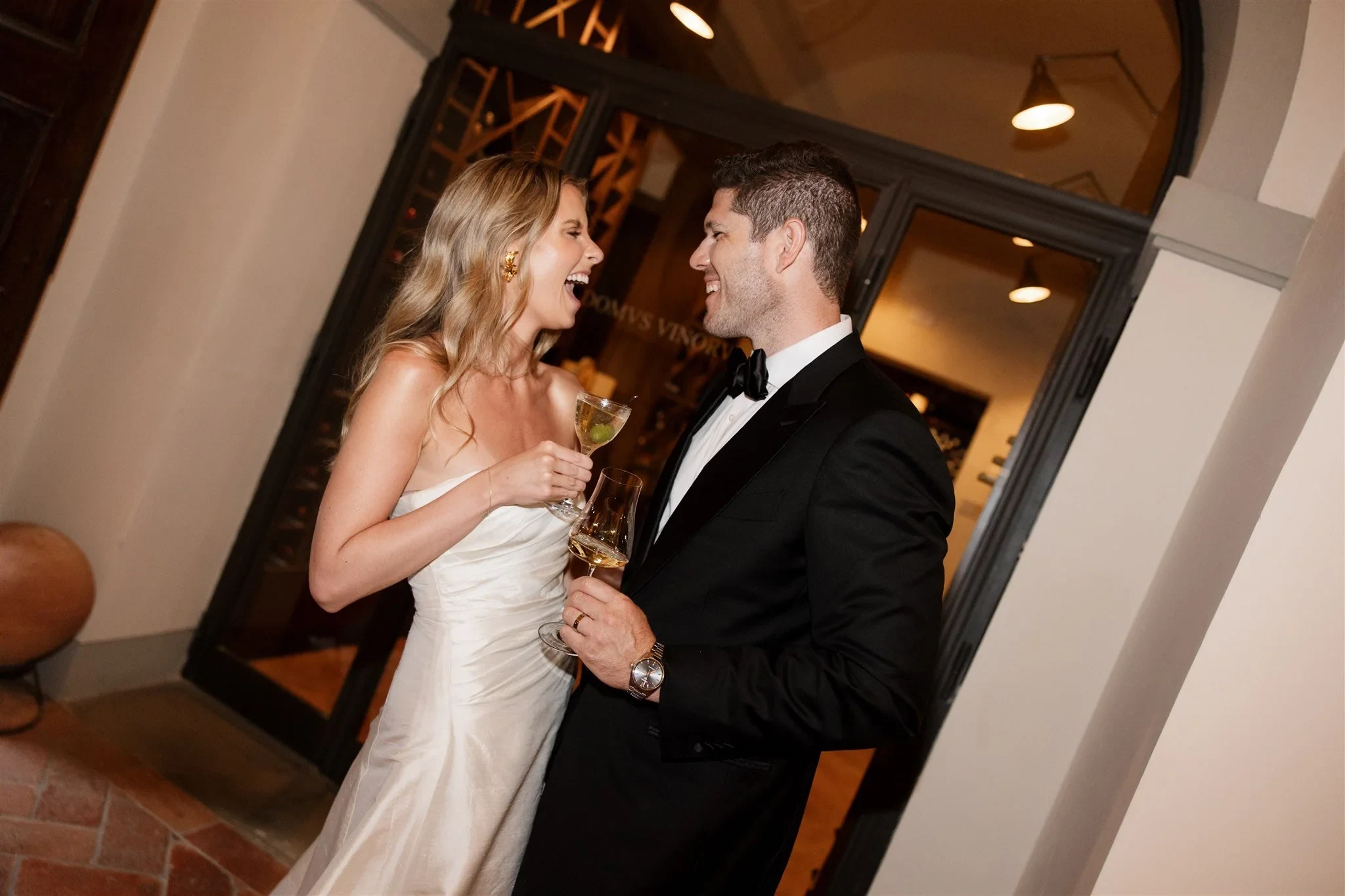 Couple in wedding attire holding drinks indoors