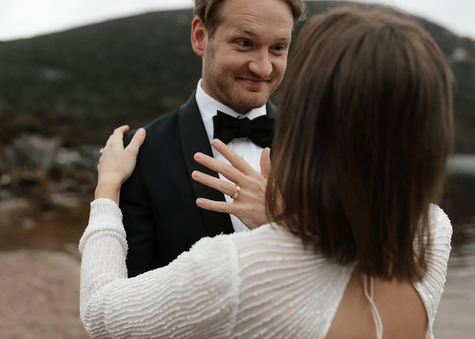 Josh smiling at April as she lifts her hands towards his shoulders, showing her wedding ring, at Dove Lake, Cradle Mountain, Tasmania, for an Elopement Collective elopement. Photo by Bulb Creative.
