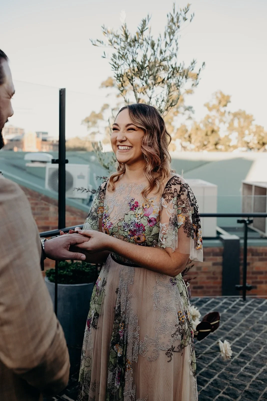 Victoria smiling as she holds Daniel’s hand during their rooftop ceremony, at Agnes Restaurant in Fortitude Valley, Brisbane, for an Elopement Collective elopement. Photo by Tessa Shannon.