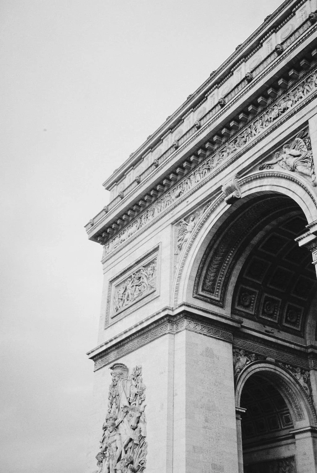 Black and white photo of the Arc de Triomphe in Paris, featuring detailed sculptures and architectural elements.