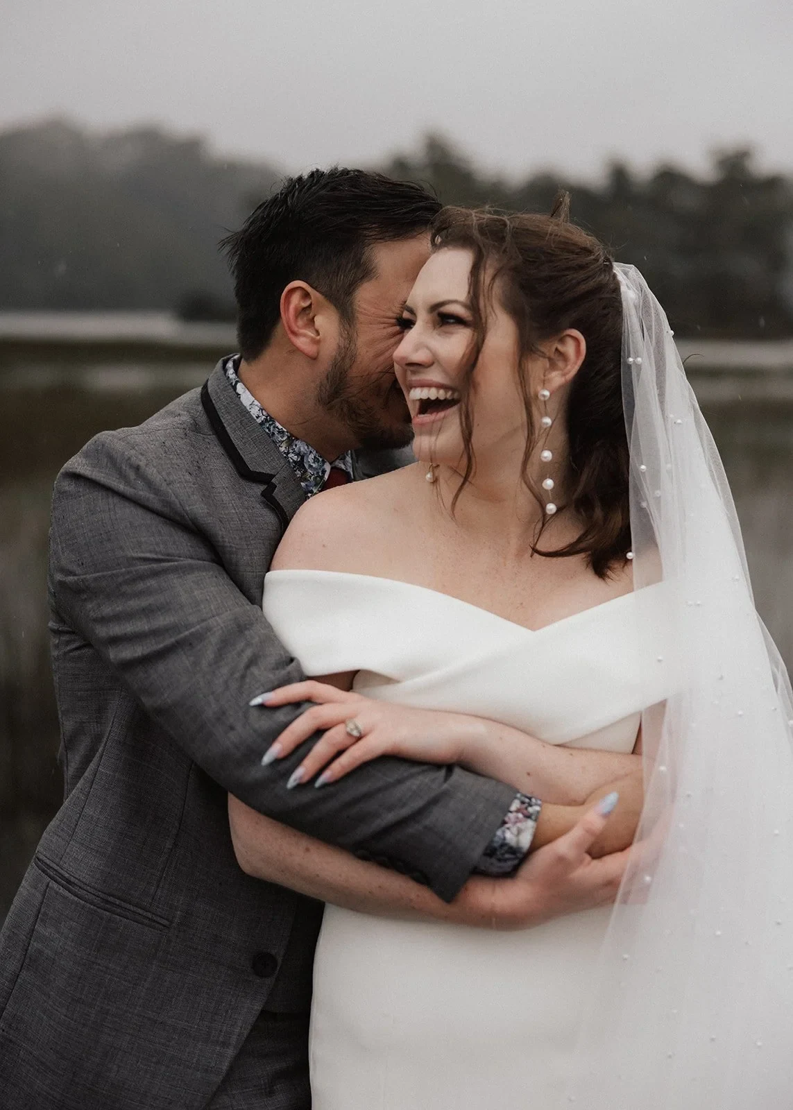 Sarah laughing as Jono kisses her cheek beside the lake, at Pumphouse Point, Lake St Clair, Tasmania, for an Elopement Collective elopement. Photo by Bulb Creative.