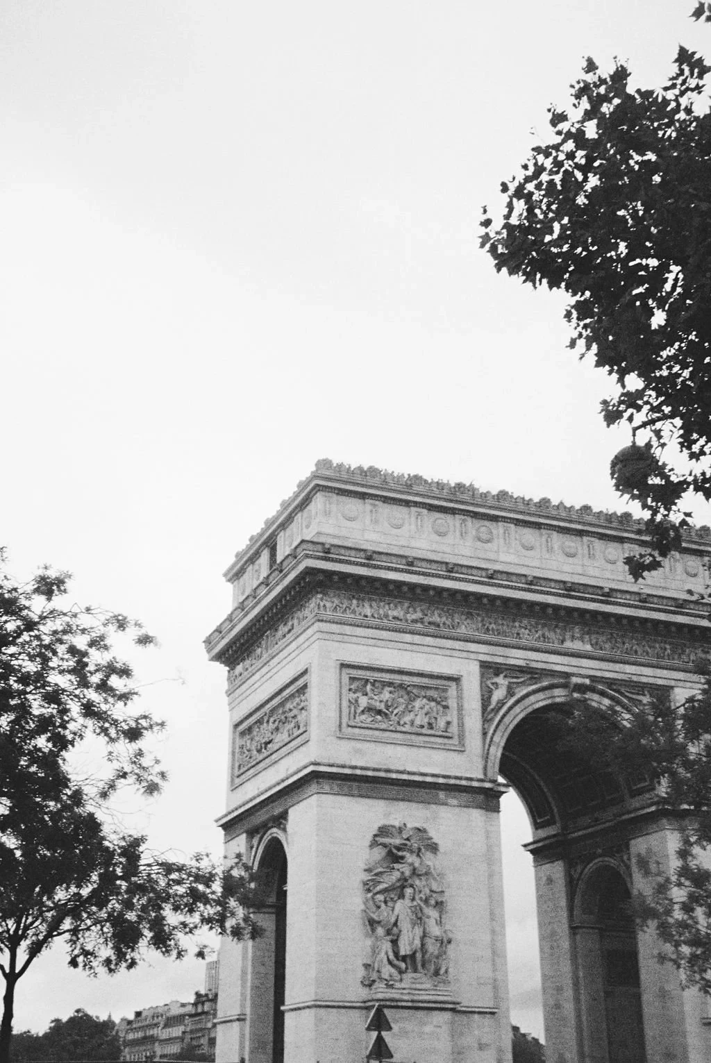 Black and white photo of the Arc de Triomphe in Paris, partially obscured by trees.