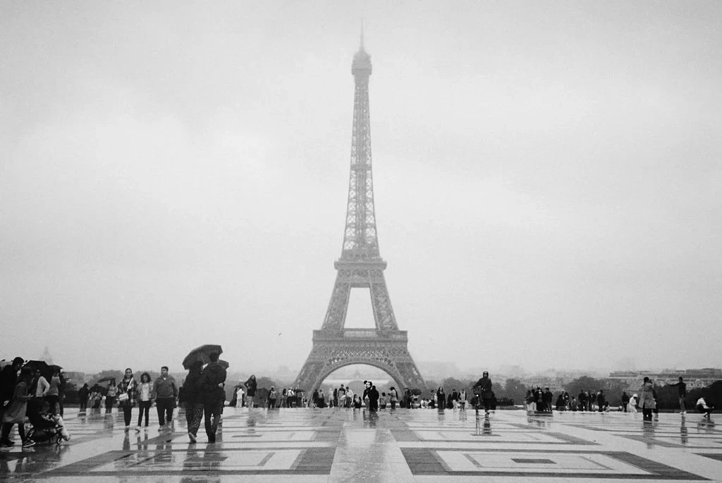 Eiffel Tower in black and white, people walking and holding umbrellas in foreground