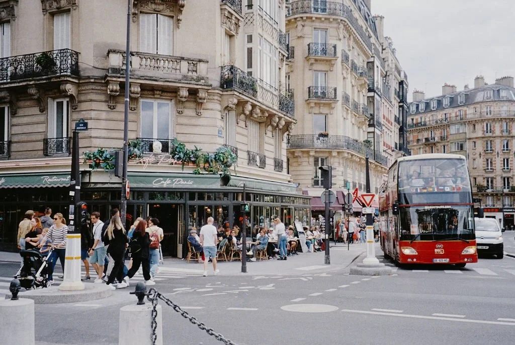 Busy Paris street corner with a cafe, pedestrians, and a red double-decker bus, from an elopement in Europe.