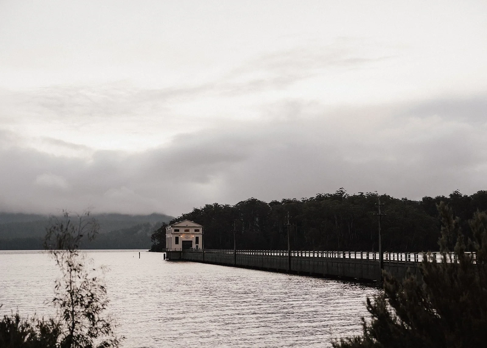The Pumphouse Point building at the end of its long jetty, with forested hills across the lake, at Pumphouse Point, Lake St Clair, Tasmania, for an Elopement Collective elopement. Photo by Bulb Creative.