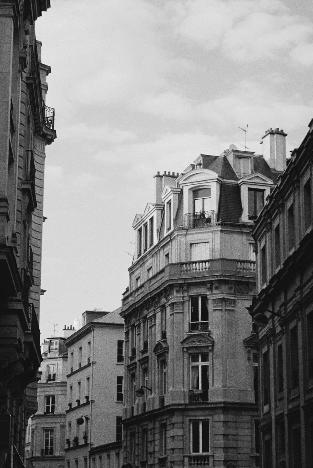 Black and white photo of Parisian-style buildings with balconies and ornate facades against a cloudy sky.