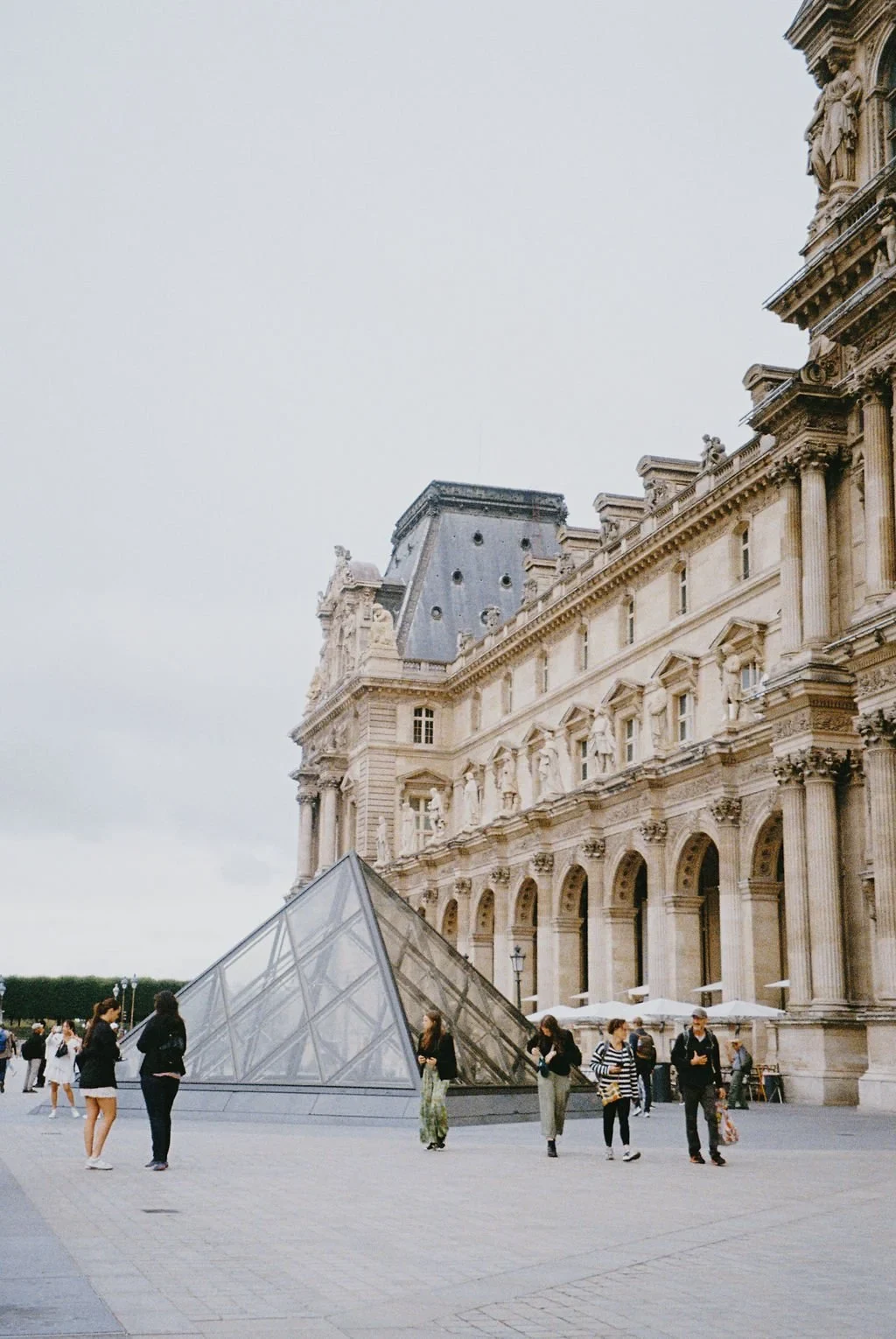Louvre Museum with glass pyramid entrance and people walking outside.