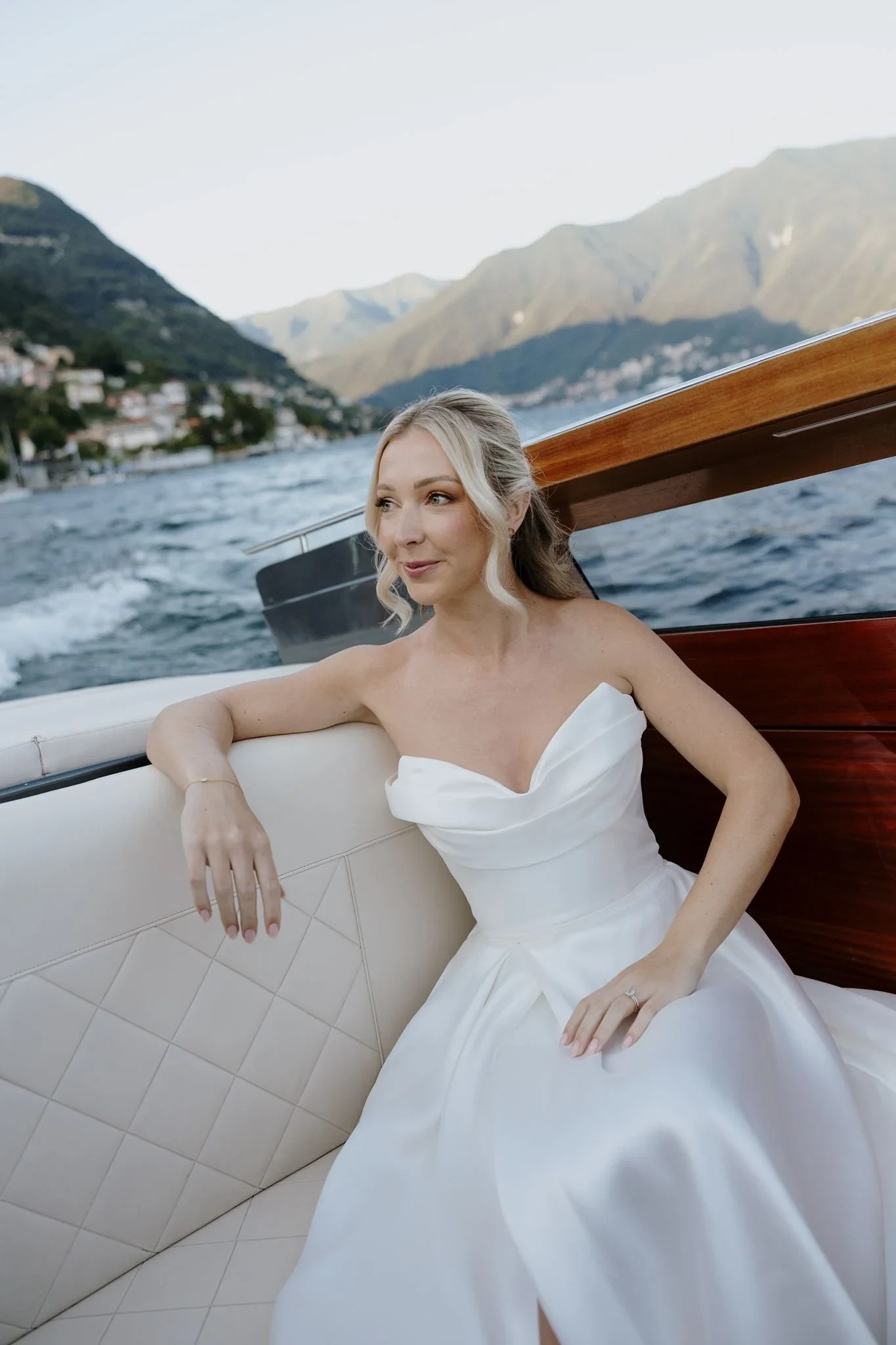 Bride in a white dress seated in a wooden boat on a mountain lake